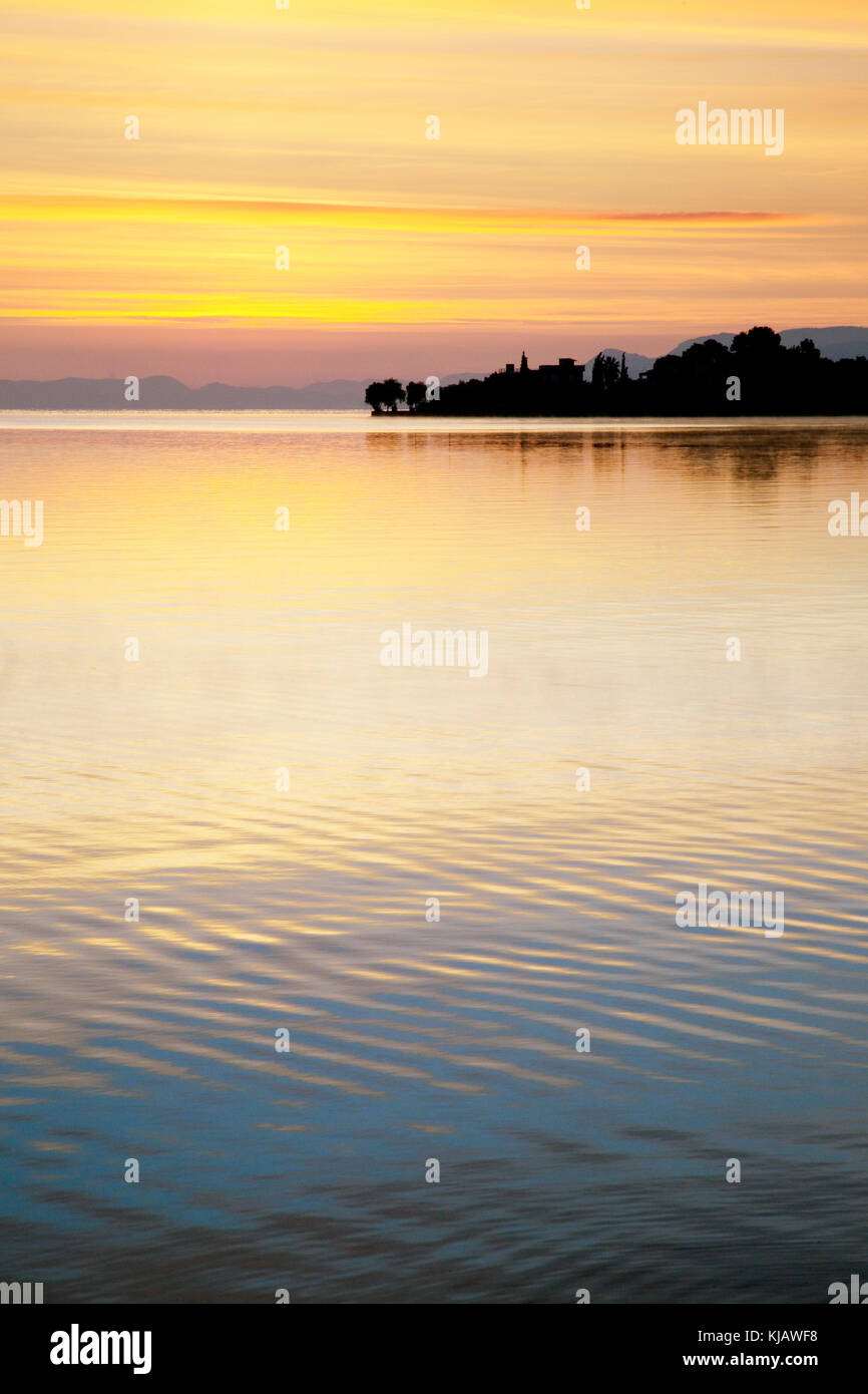 Before sunrise the colorful sky is reflected in the gentle ripples of a calm sea. Stock Photo