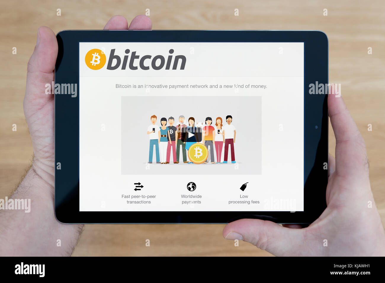 A man looks at the Bitcoin website on his iPad tablet device, shot against a wooden table top background (Editorial use only) Stock Photo