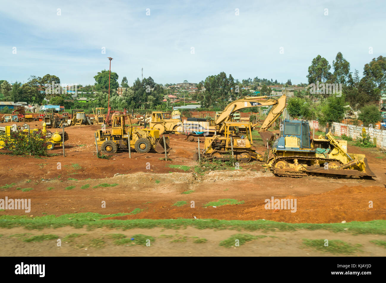 Several construction vehicles sit in an open yard by the roadside, Kenya, East Africa Stock Photo