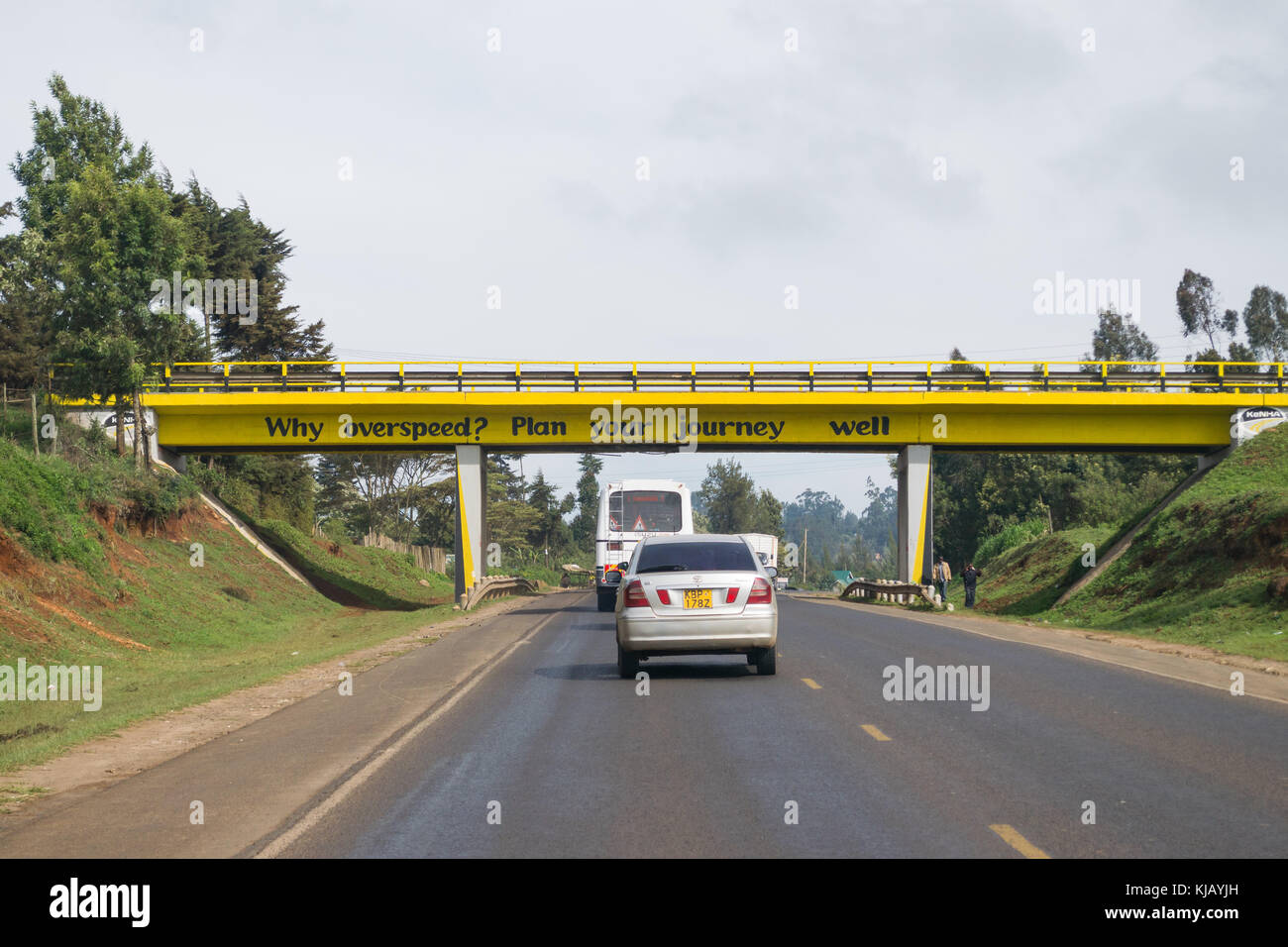 Cars and vehicles pass under a bridge with advice on speeding written on it, Kenya, East Africa Stock Photo
