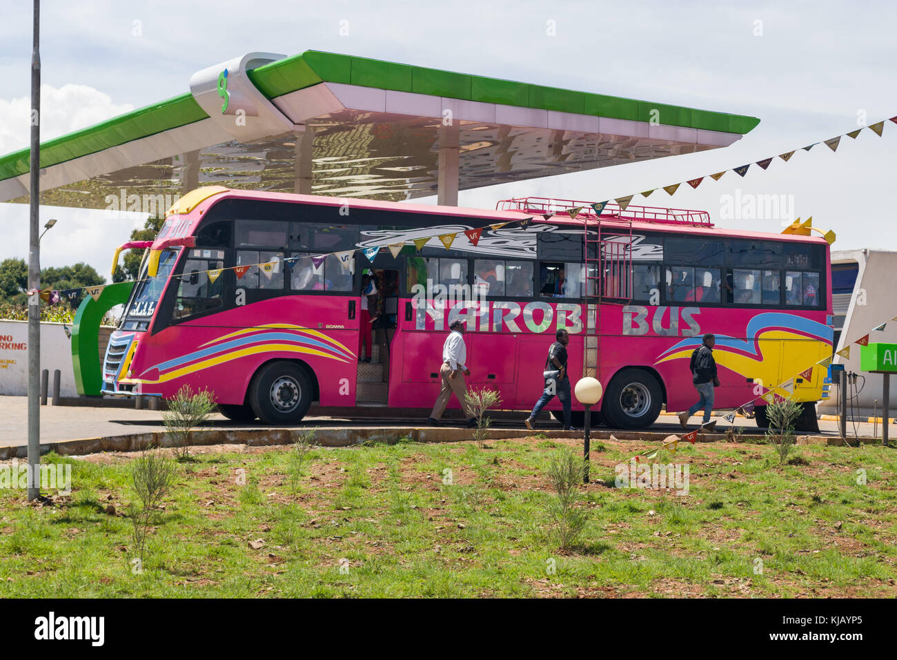 A brightly coloured bus stopped at a petrol station rest stop with people walking alongside, Kenya, East Africa Stock Photo