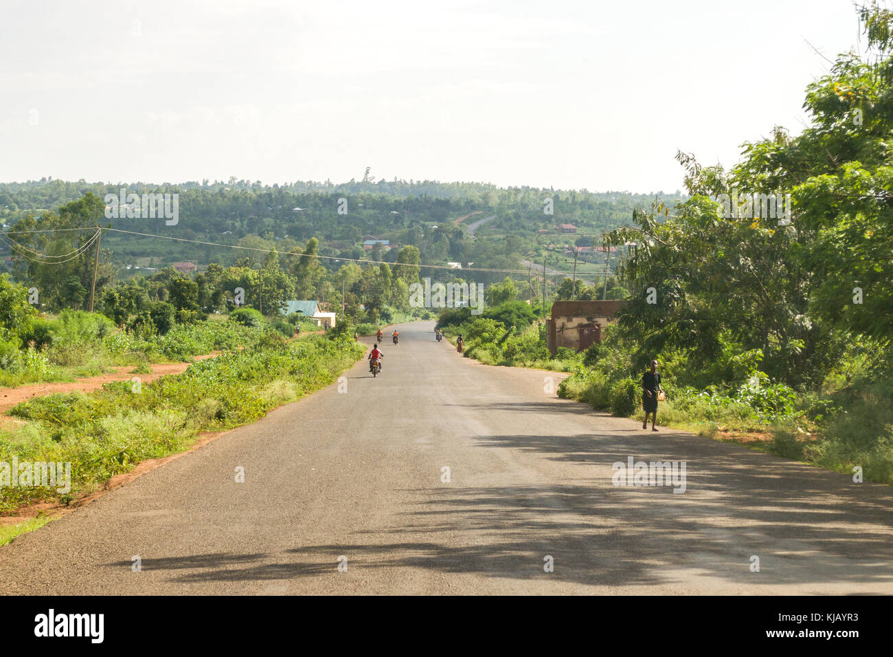 A wide dual carriageway road running through countryside with vehicles and people on it, Kenya, East Africa Stock Photo