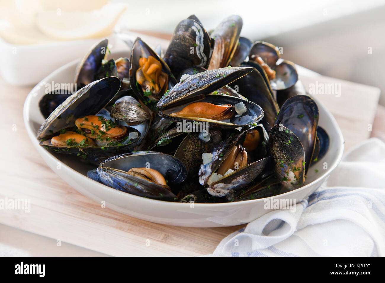 Cooked mussels in white bowl on wooden base Stock Photo