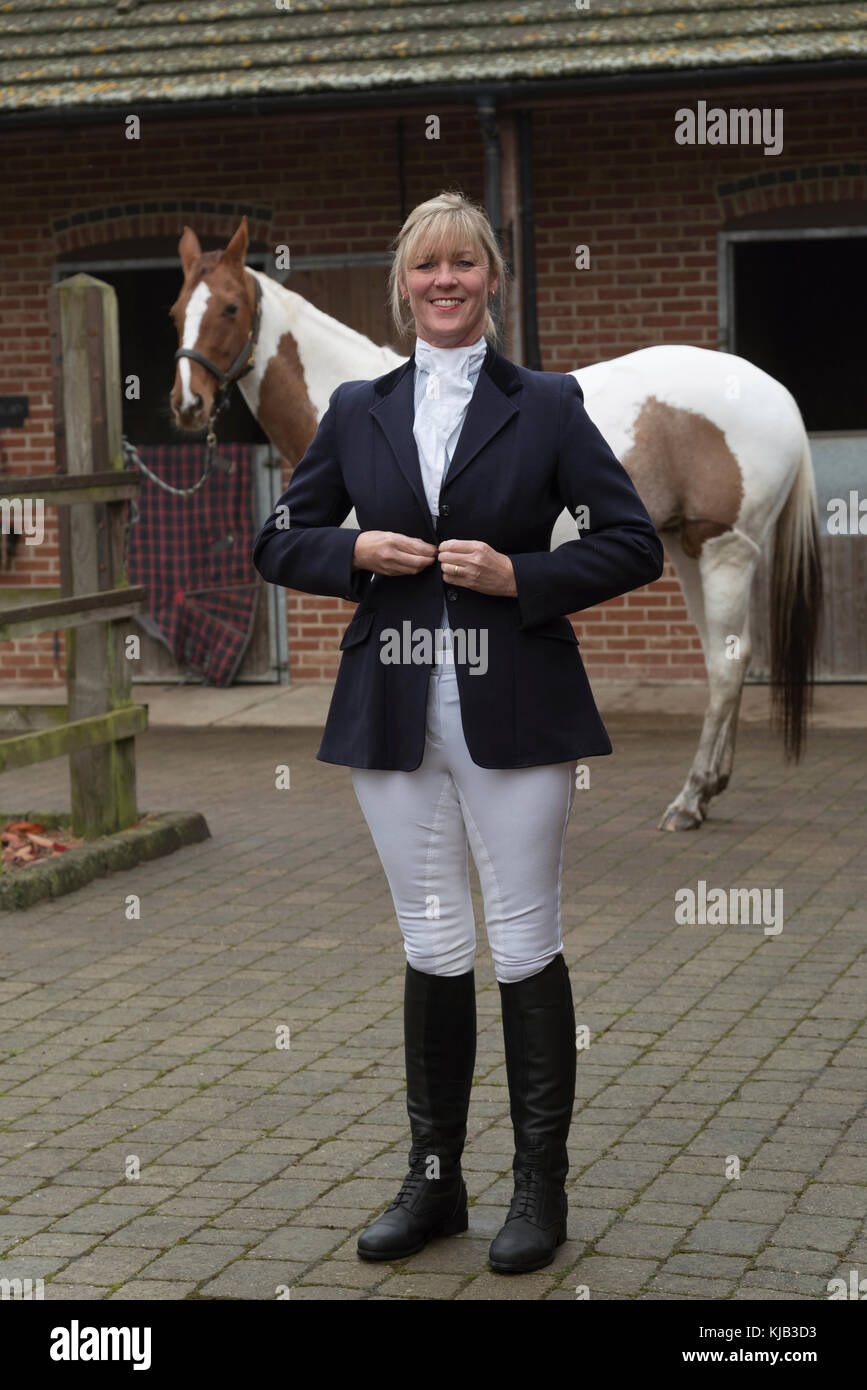 Smartly dressed horse rider buttoning a dark blue riding jacket ...