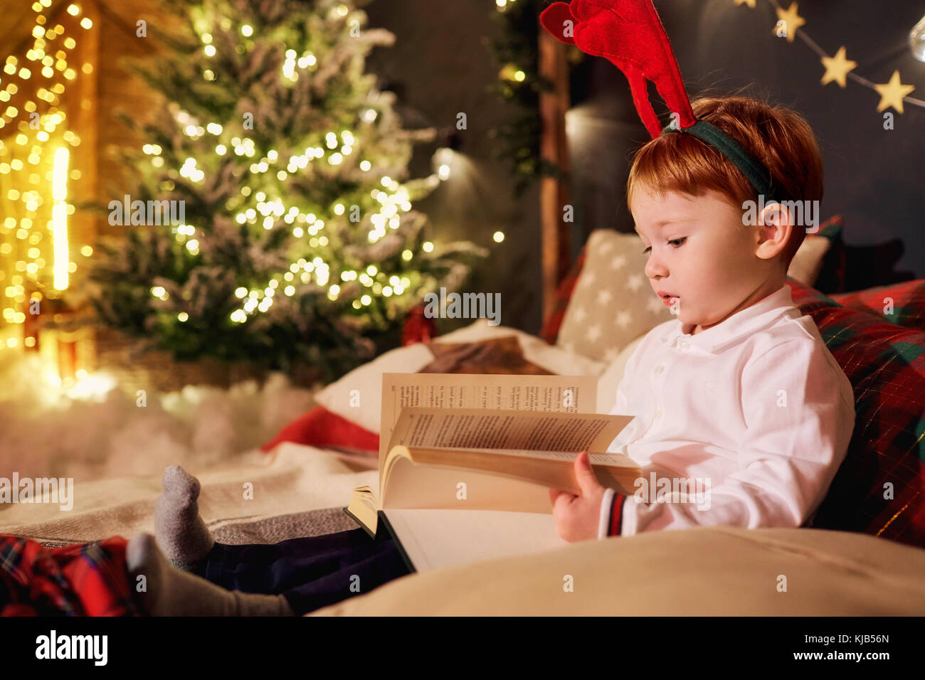 A little boy is reading a book in the Christmas room. Stock Photo