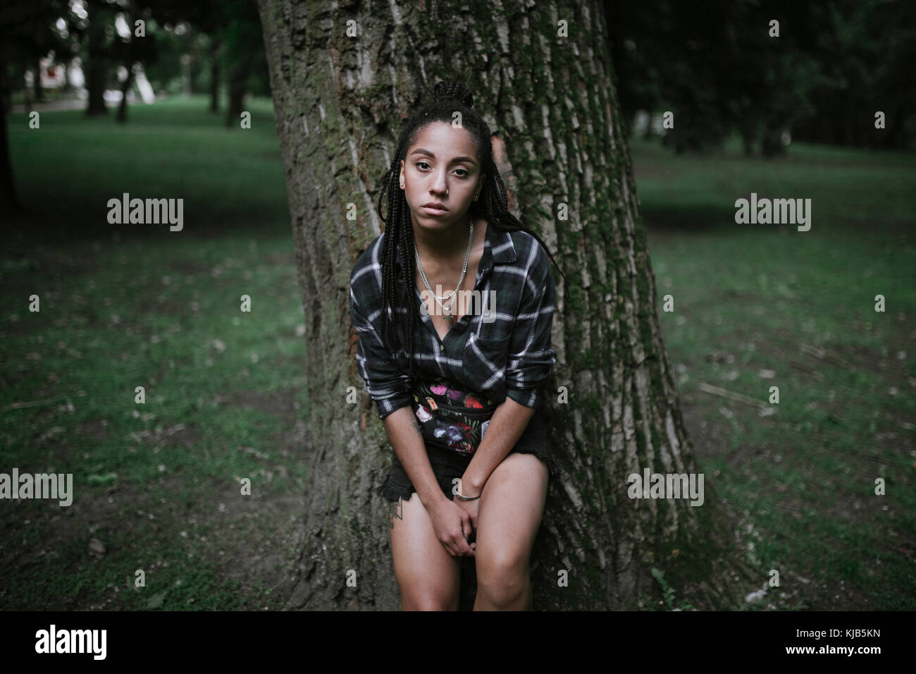 Portrait of serious African American woman leaning on tree Stock Photo