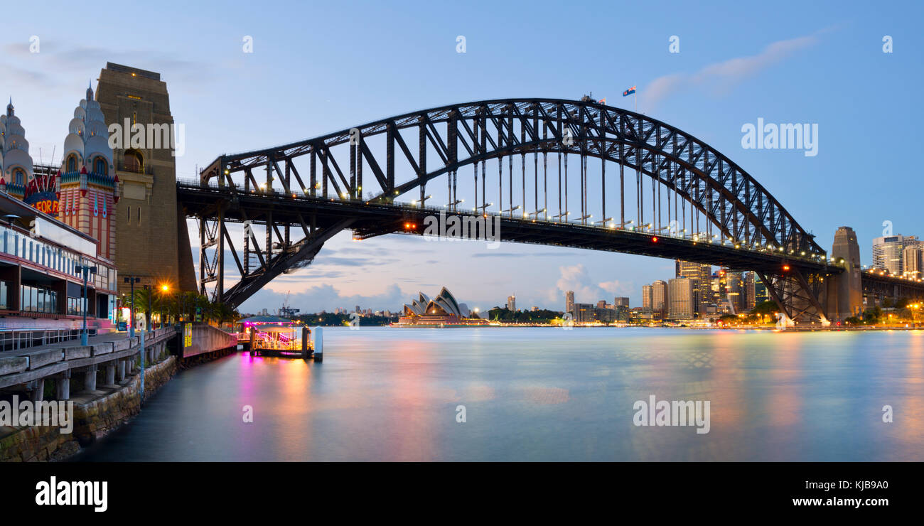 Panoramic photography of the Harbour Bridge and the Sydney Opera House from Luna Park in Milsons Point, Sydney, NSW, Australia right before sunrise. Stock Photo