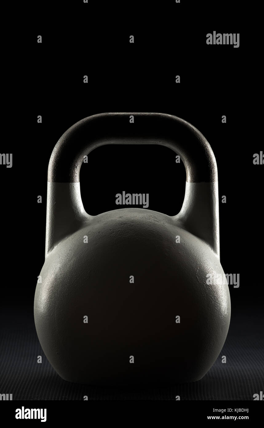 Side lit competition kettlebell silhouette on a weight training gym floor with potential text / writing / copy space on and above kettlebell Stock Photo