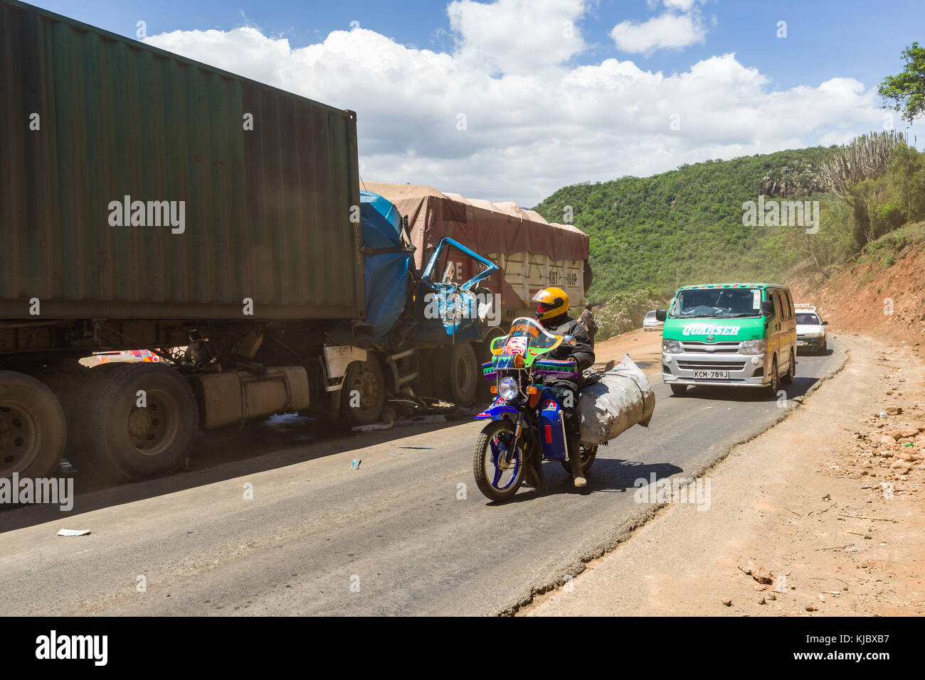 Vehicles drive past the aftermath of a road traffic accident involving two lorries on a Rift Valley road, Kenya, East Africa Stock Photo