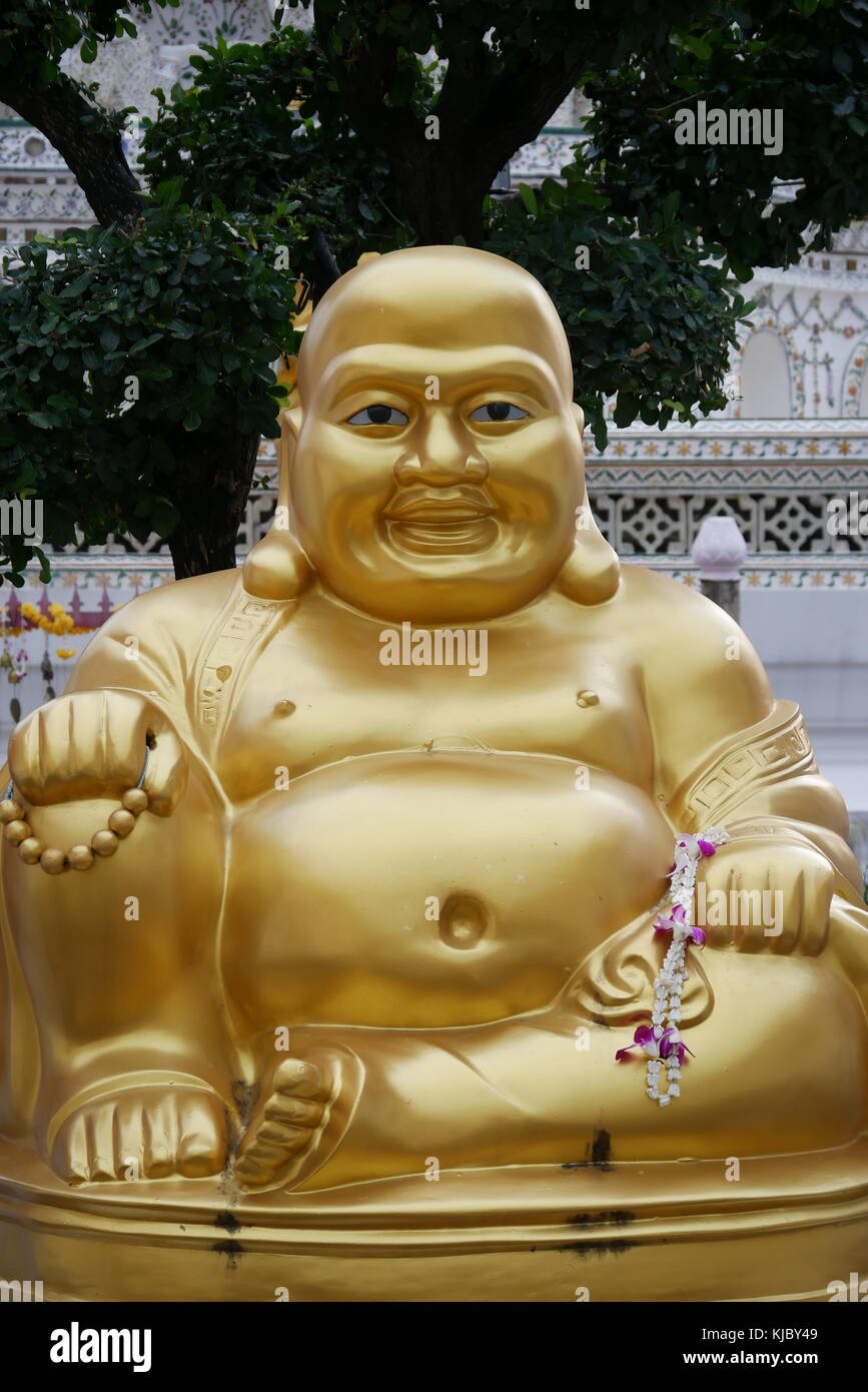 A Laughing Buddha golden statue, a Chinese deity known as Budai, Hotei or Pu-Tai, sits in front of Wat Arun temple in Bangkok. Stock Photo