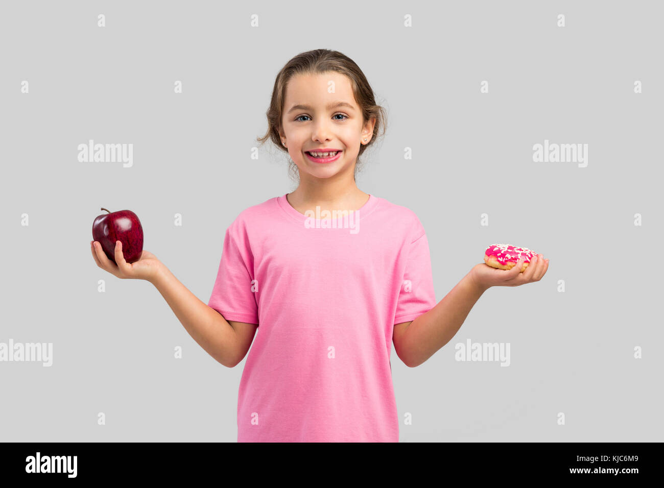 Little girl smiling and choosing between a apple and a donut Stock Photo