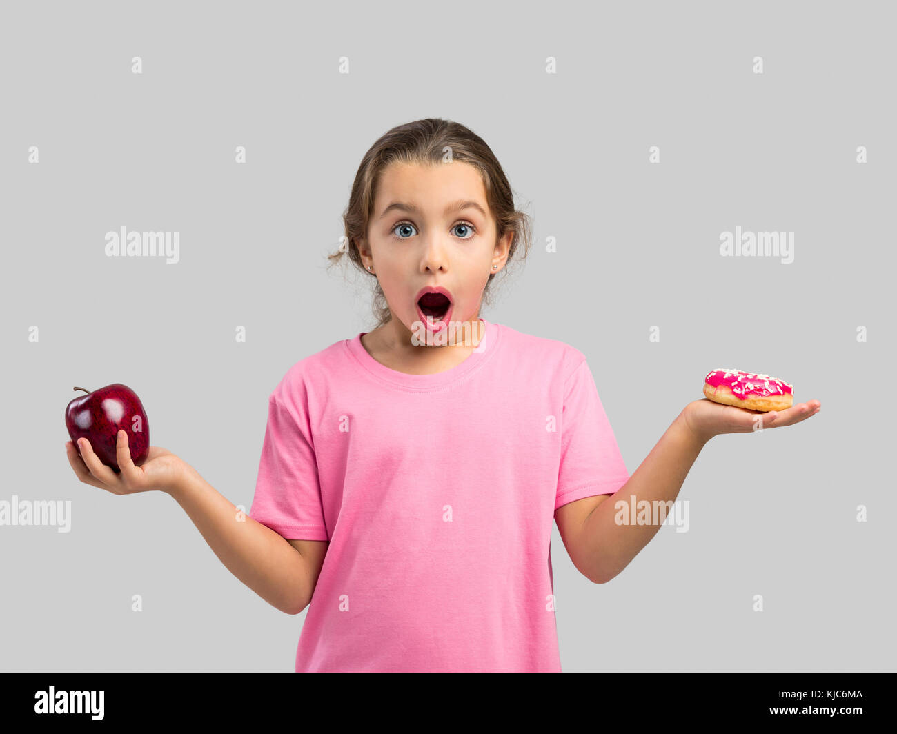 Little girl smiling and choosing between a apple and a donut Stock Photo