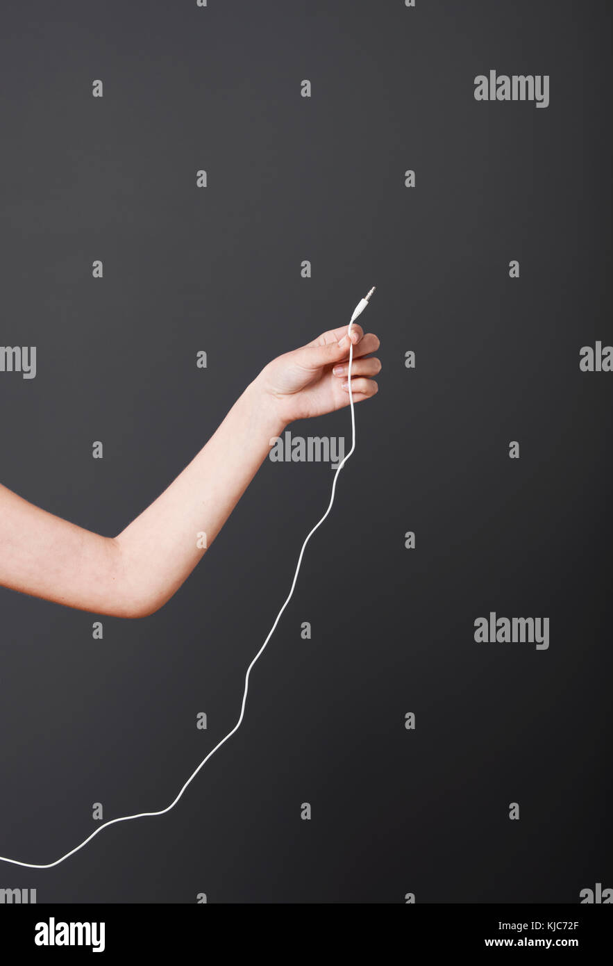 Hand holding a stereo audio cable over a gray background Stock Photo