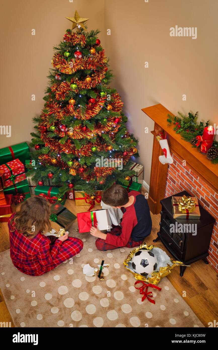 Overhead view of Children opening their gift wrapped presents on Christmas morning sitting next to the tree and fireplace. Stock Photo