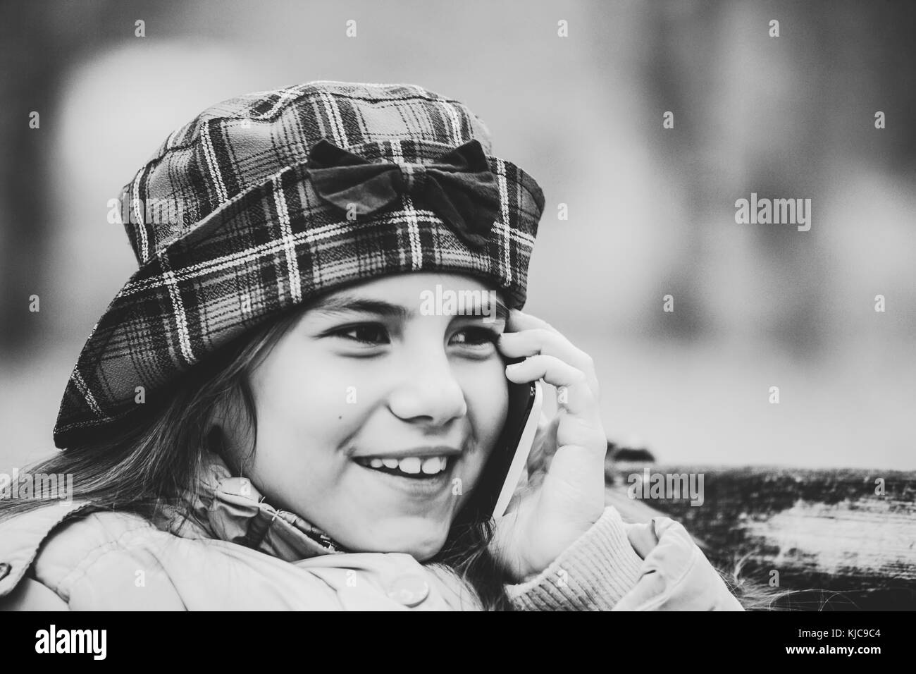 Close up face shot of cute little girl with hat talking on smart phone outdoor.Kid with smartphone. Kids and technology concept. Black and white photo Stock Photo