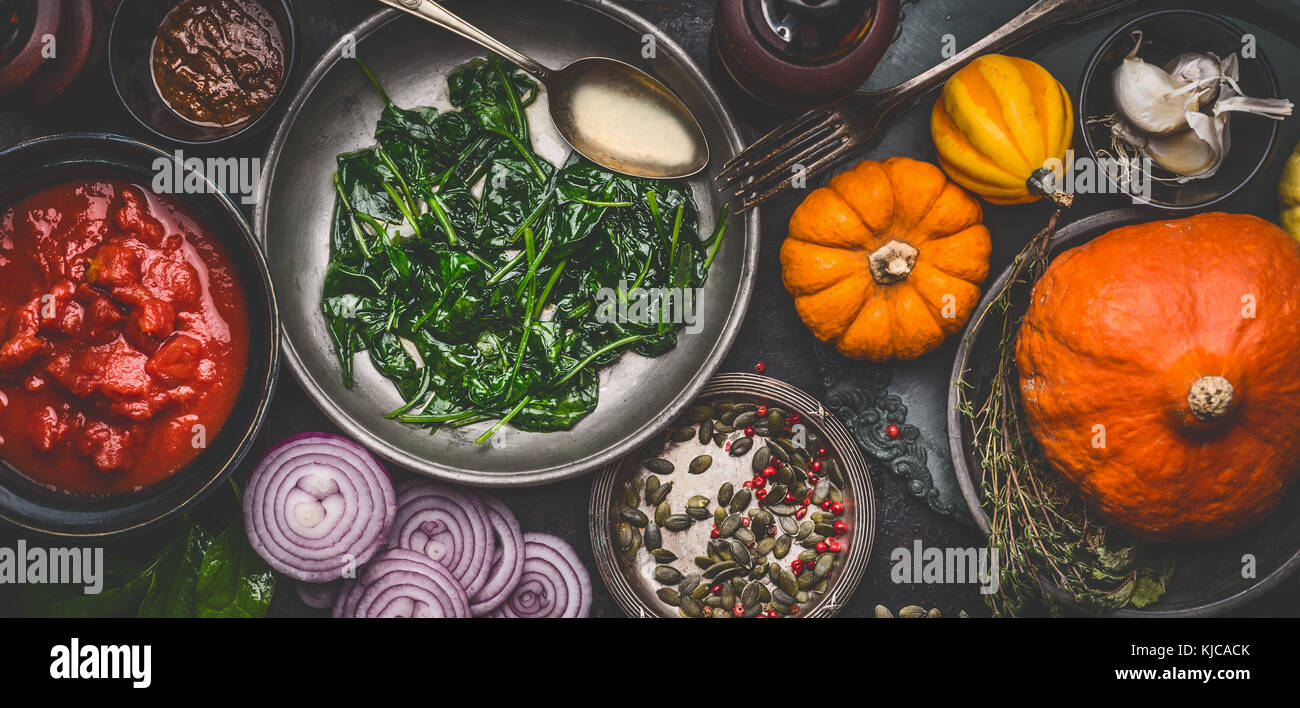 Healthy vegetarian cooking ingredients for tasty pumpkin dishes recipes in bowls : tomato sauces, spinach, sliced onion, pumpkin seeds, top view, bann Stock Photo