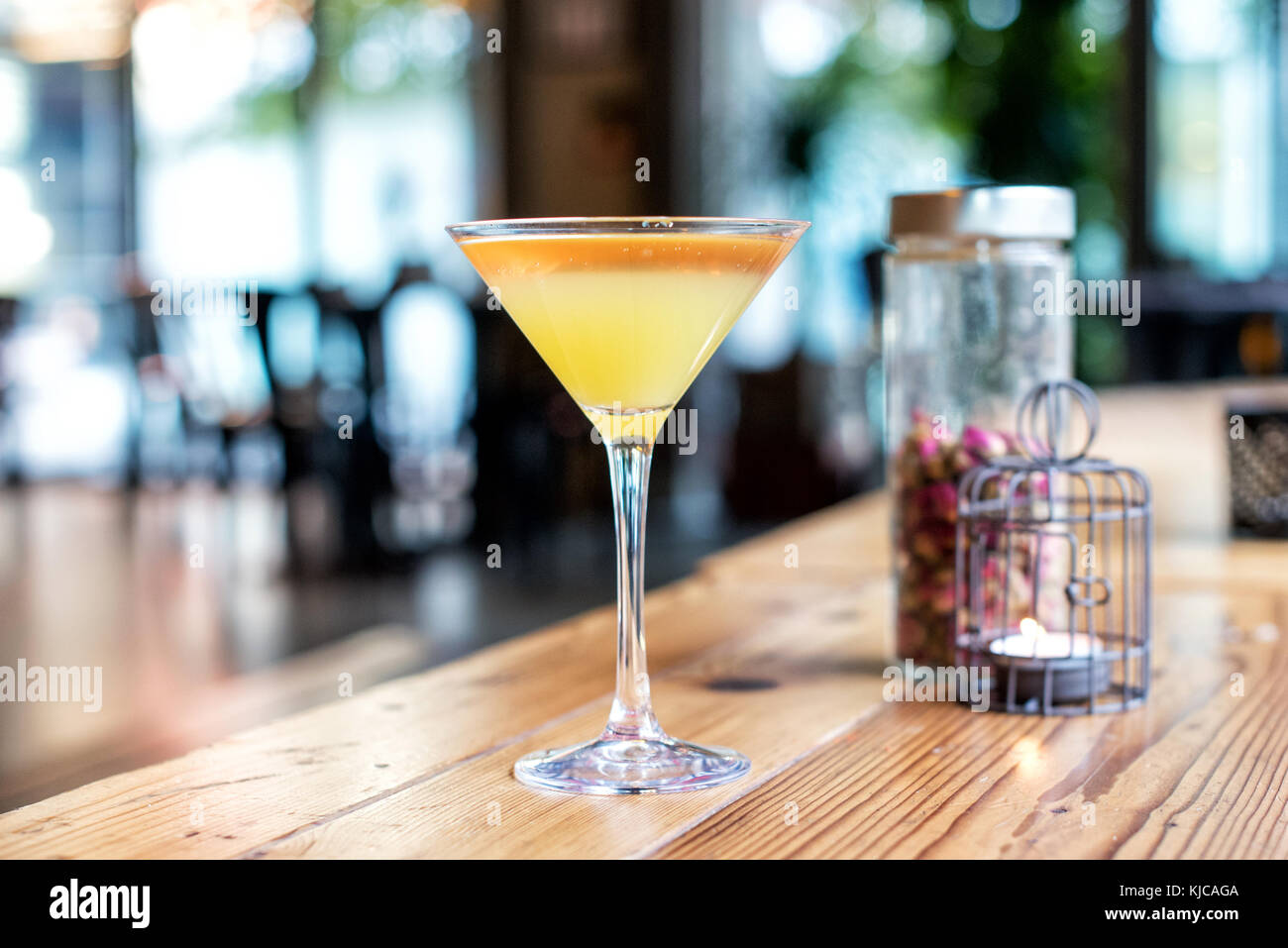 Close-up of a sweet yellow alcoholic cocktail in a stemmed glass on wood countertop in the interior of a bar Stock Photo