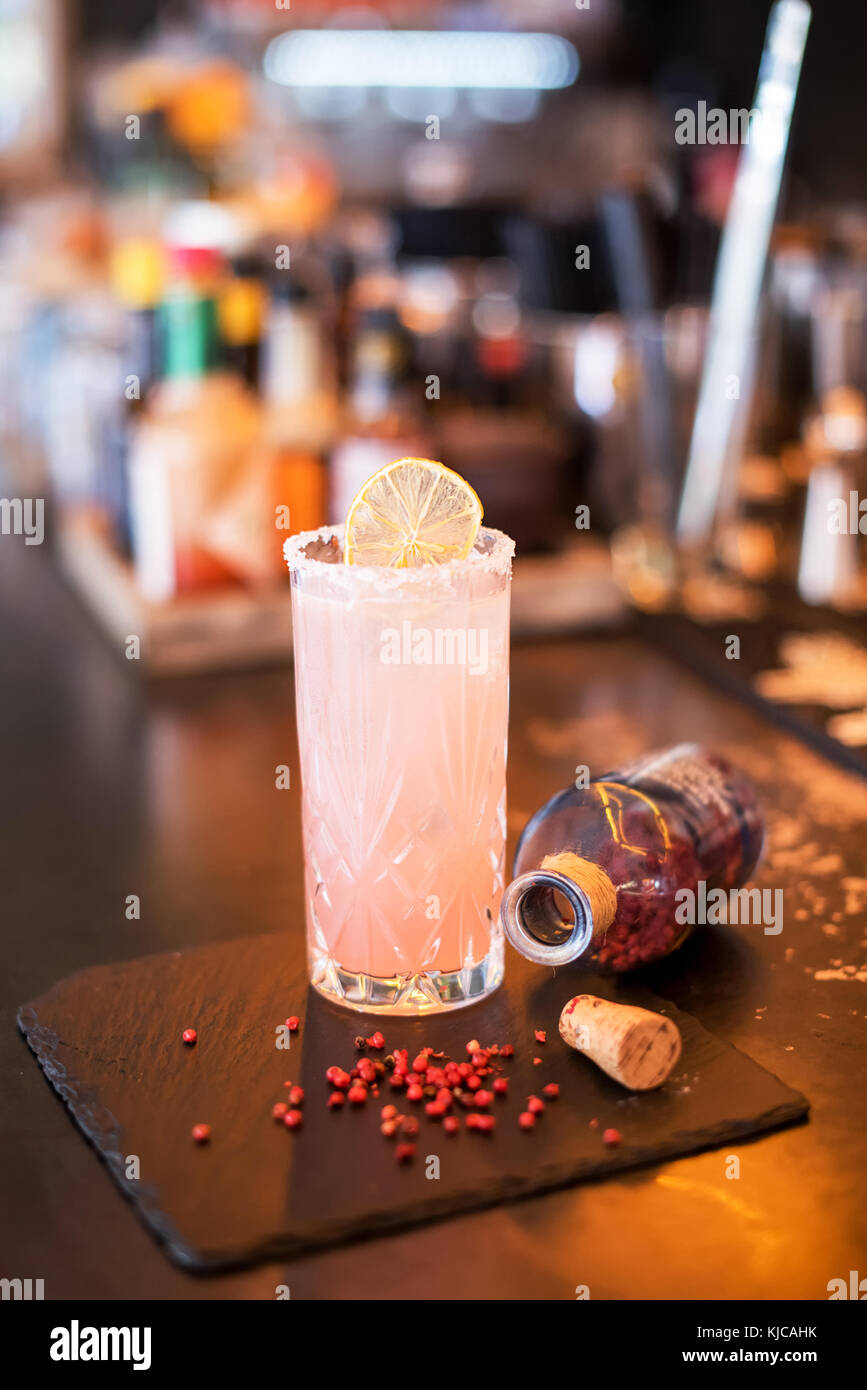 Chilled blended alcoholic cocktail with pomegranate served in a tall glass with sugar frosted rim on a wooden bar counter with open bottle and ingredi Stock Photo