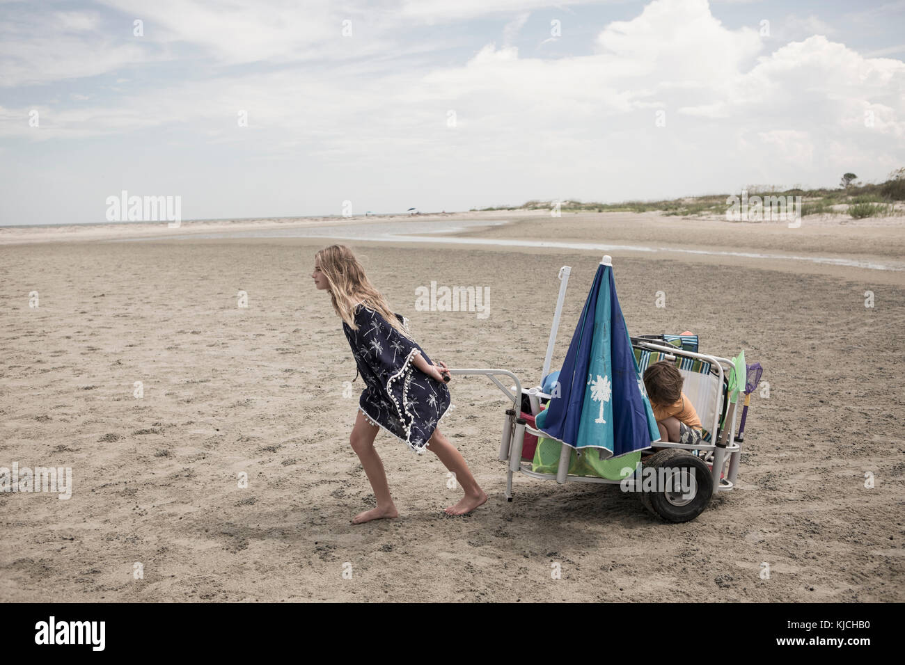 Girl pulling brother in cart on beach Stock Photo
