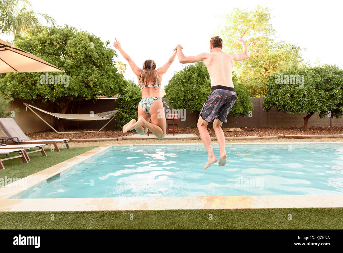 Caucasian couple holding hands jumping into swimming pool Stock Photo