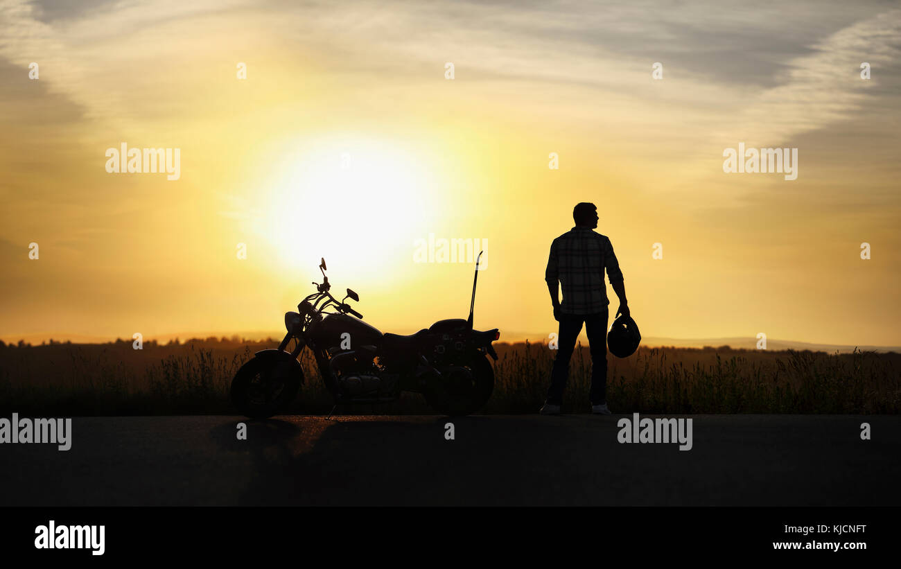 Silhouette of man holding helmet near motorcycle at sunset Stock Photo
