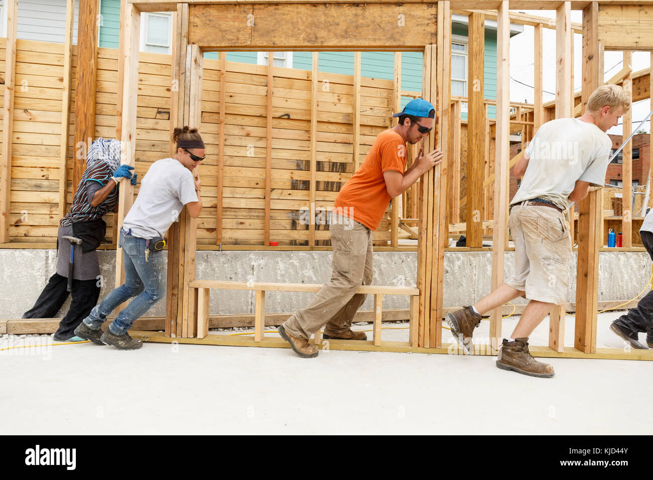 Volunteers pushing framed wall at construction site Stock Photo
