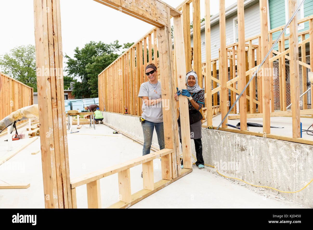 Smiling volunteers holding framed wall at construction site Stock Photo