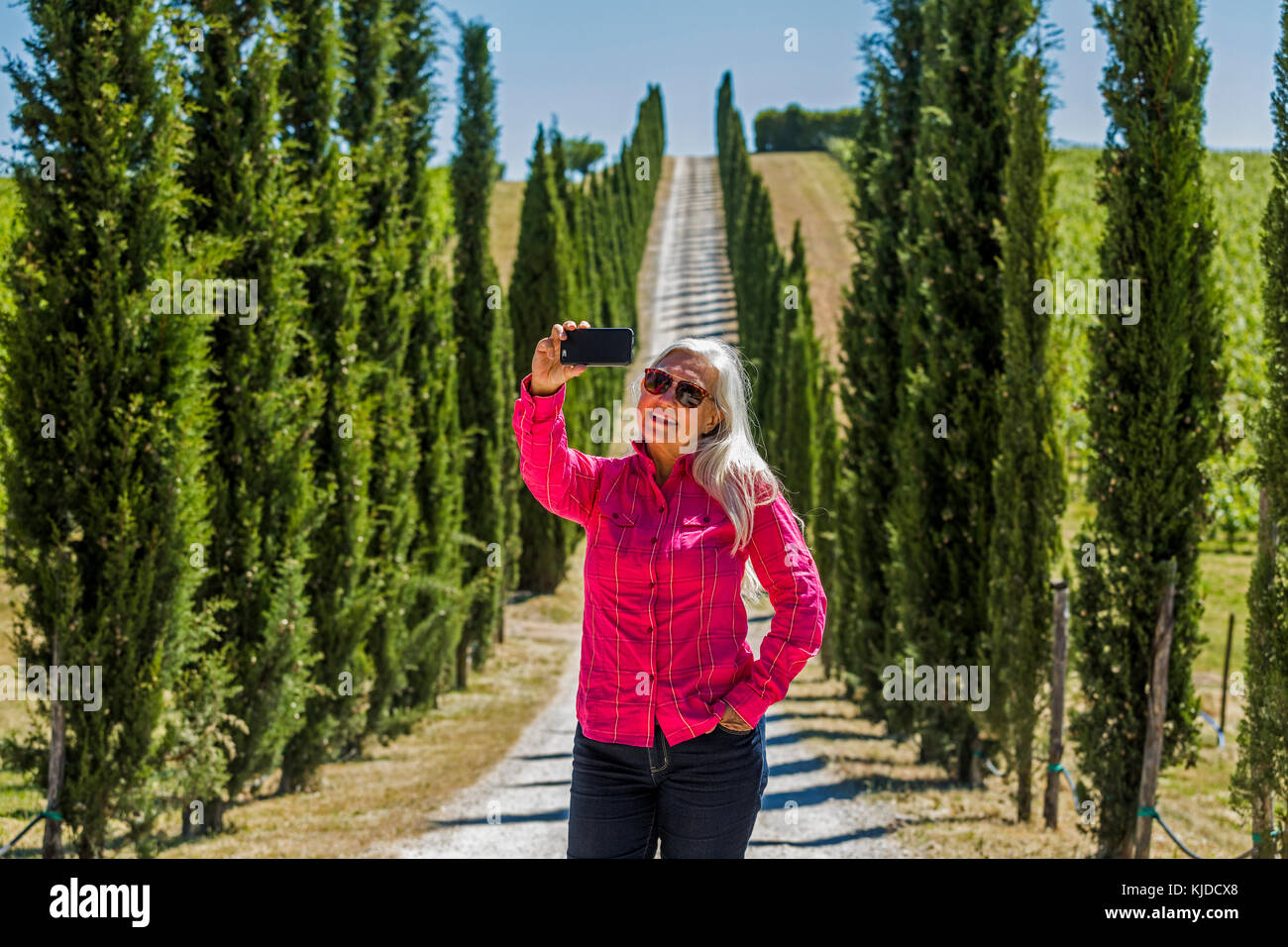 Caucasian woman posing for cell phone selfie on dirt road Stock Photo