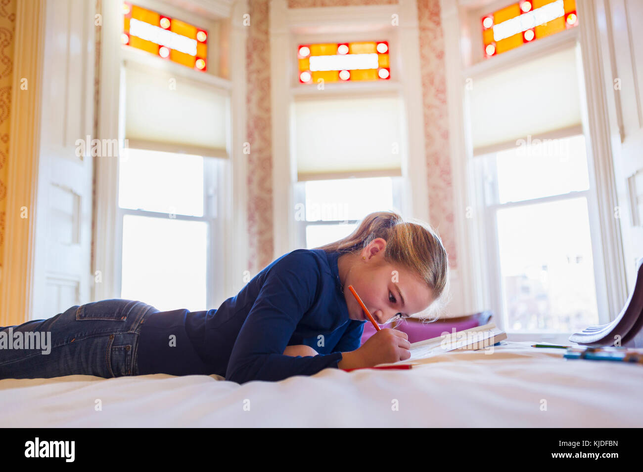Caucasian girl laying on bed writing in notebook Stock Photo