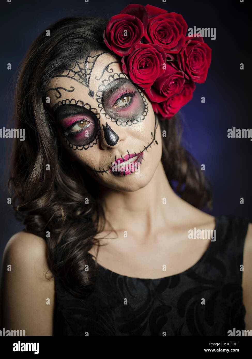 Beautiful Mexican American woman celebrating Día de los Muertos ( Día de Muertos ) is the Mexican holiday also known as Day of the Dead with skull makeup and roses in the style of Catrina. Stock Photo