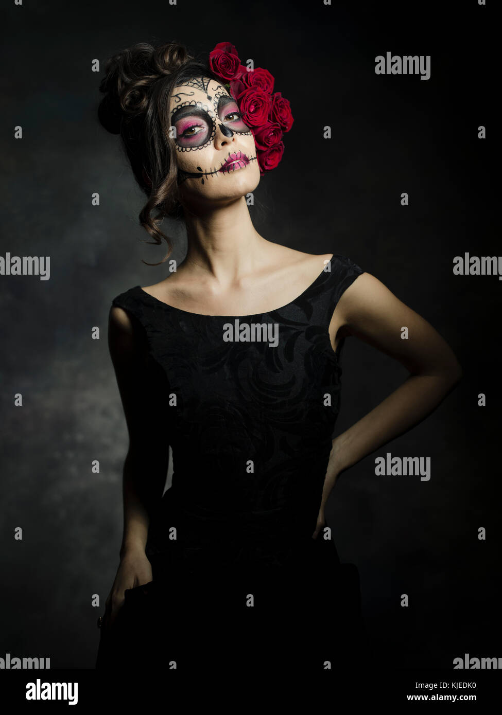 Beautiful Mexican American woman celebrating Día de los Muertos ( Día de Muertos ) is the Mexican holiday also known as Day of the Dead with skull makeup and roses in the style of Catrina. Stock Photo
