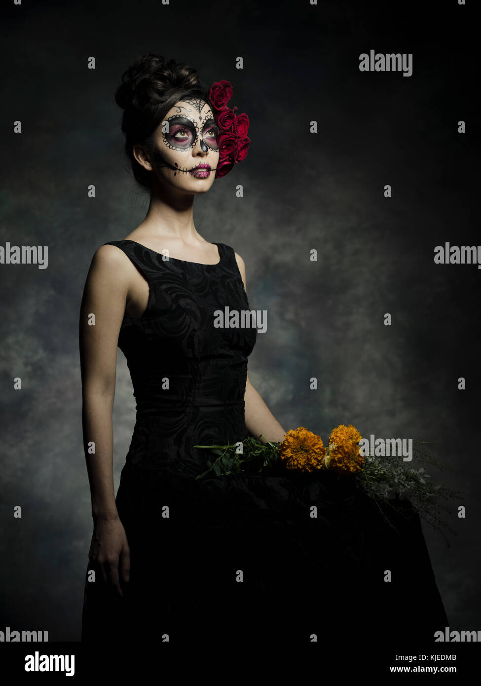 Beautiful Mexican American woman celebrating Día de los Muertos ( Día de Muertos ) is the Mexican holiday also known as Day of the Dead with skull makeup and roses in the style of Catrina. Stock Photo
