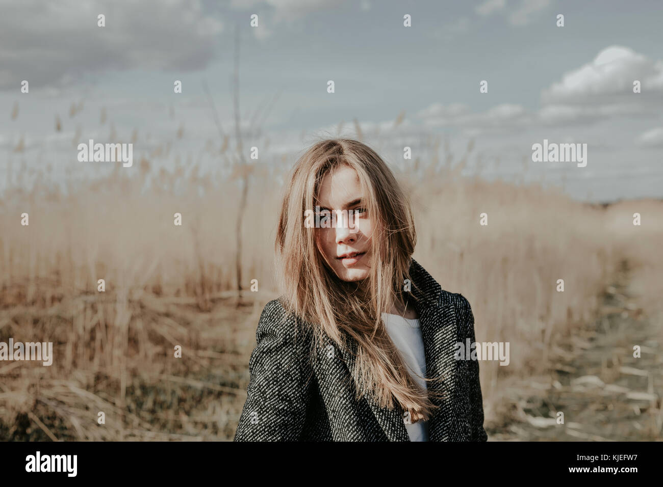 Pretty and young european woman with face covered  by her blonde hair looking at camera. Girl posing outdoor on bulrush background. Close shot. Stock Photo