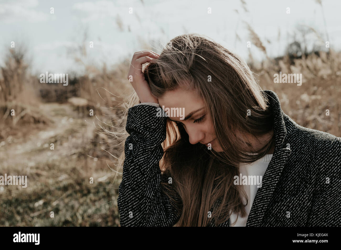 Beauty and fashion woman adjusting her hair. European girl standing on bulrush  background. Woman hold on to one's head and looking down. Wide closeup Stock Photo