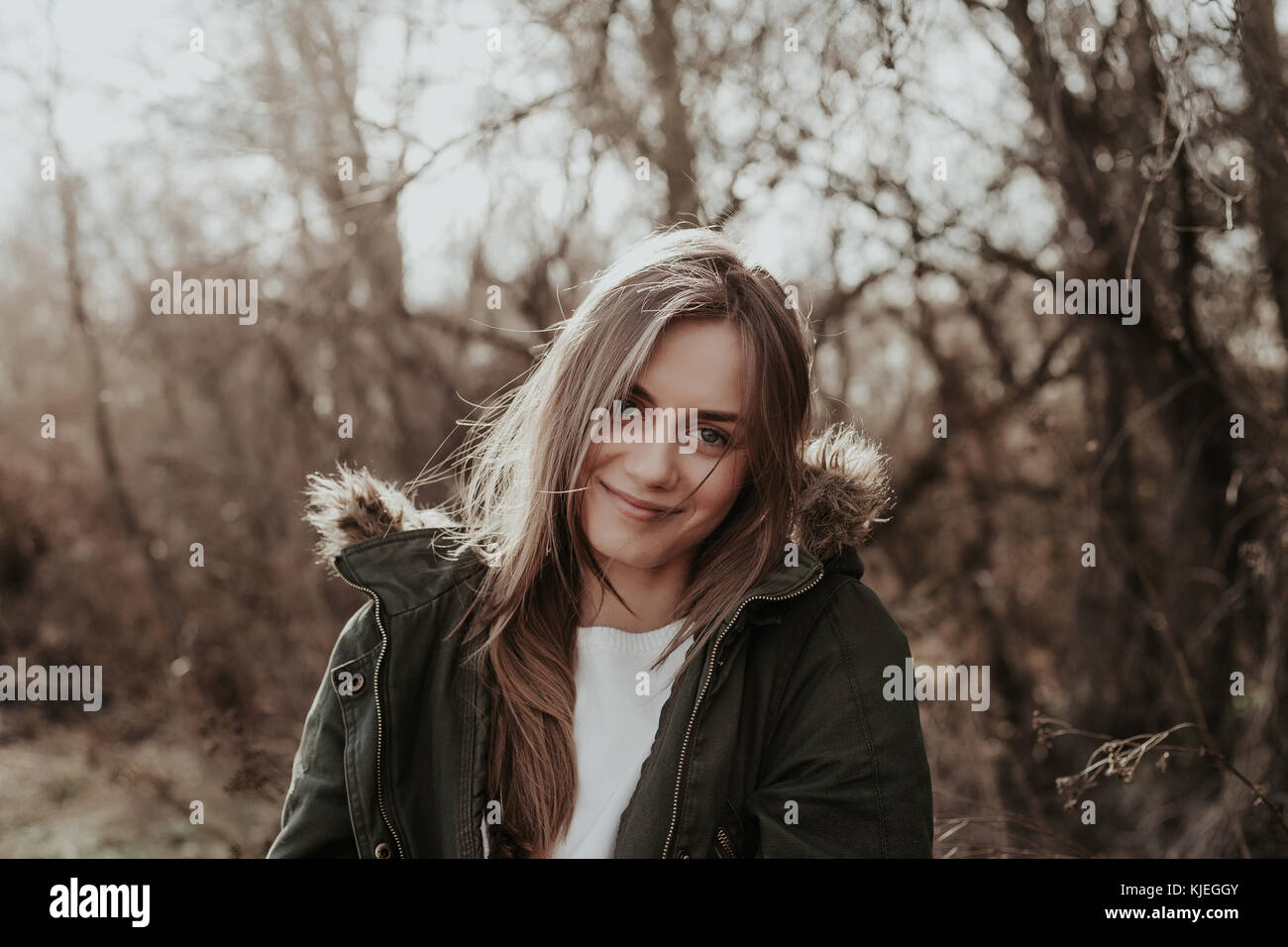 Pretty woman in warm jacket with fur posint at camera outdoor. Young european girl with long blond hair, wide eyebrows looking at camera and smiling. Stock Photo