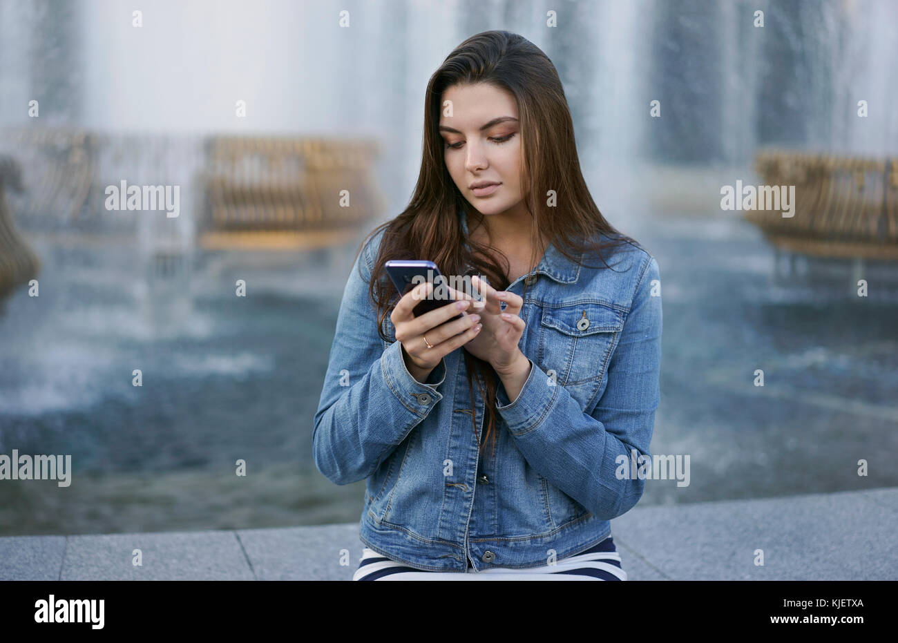 Caucasian woman texting on cell phone at fountain Stock Photo