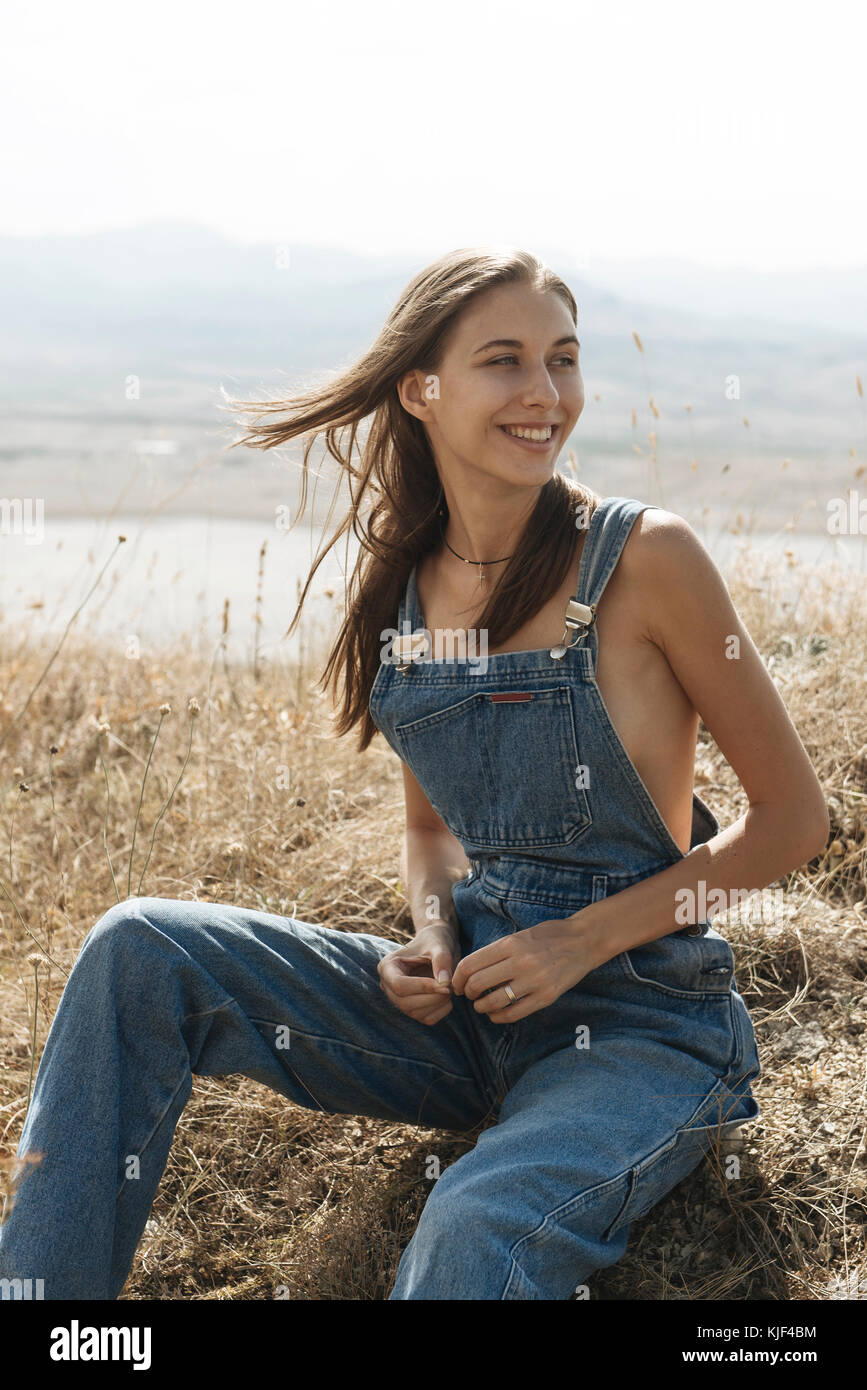 Caucasian woman wearing overalls sitting in field Stock Photo