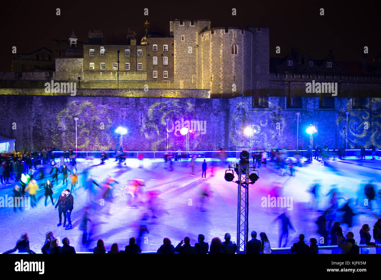 People ice skating at night on a colored ice rink in front of Tower of