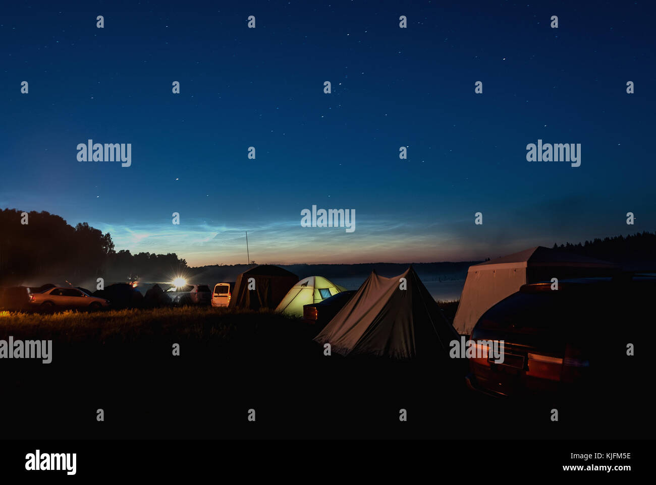 Night view of the tourist camp with tents and cars on the shore of lake on a background of the starry sky with silver clouds Stock Photo