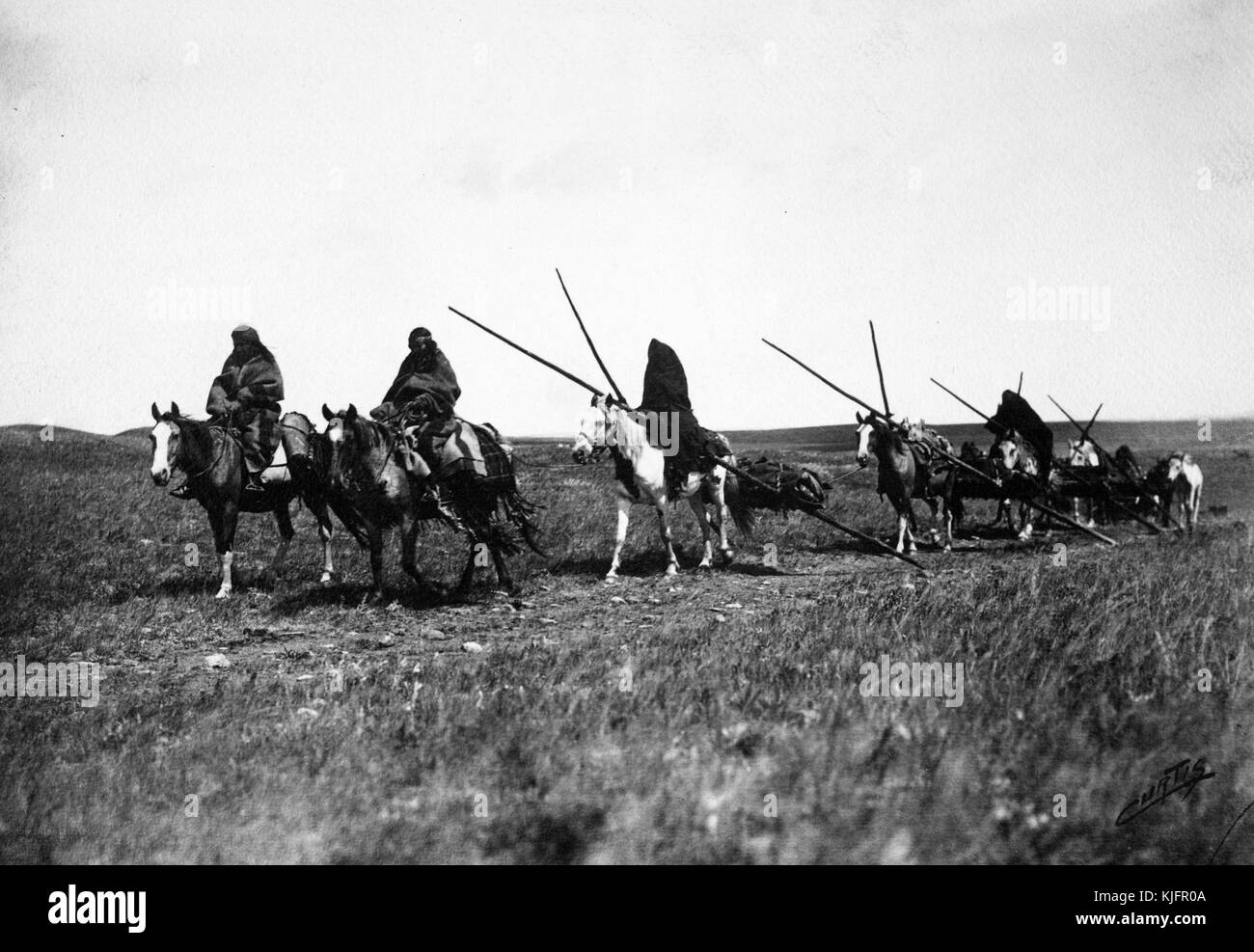 Photograph of Native American men, riding horses, traveling with their camp equipment, titled 'On the Road, a Blackfoot picture on the prairies of Montana', by Edward S Curtis, Montana, 1900. From the New York Public Library. Stock Photo