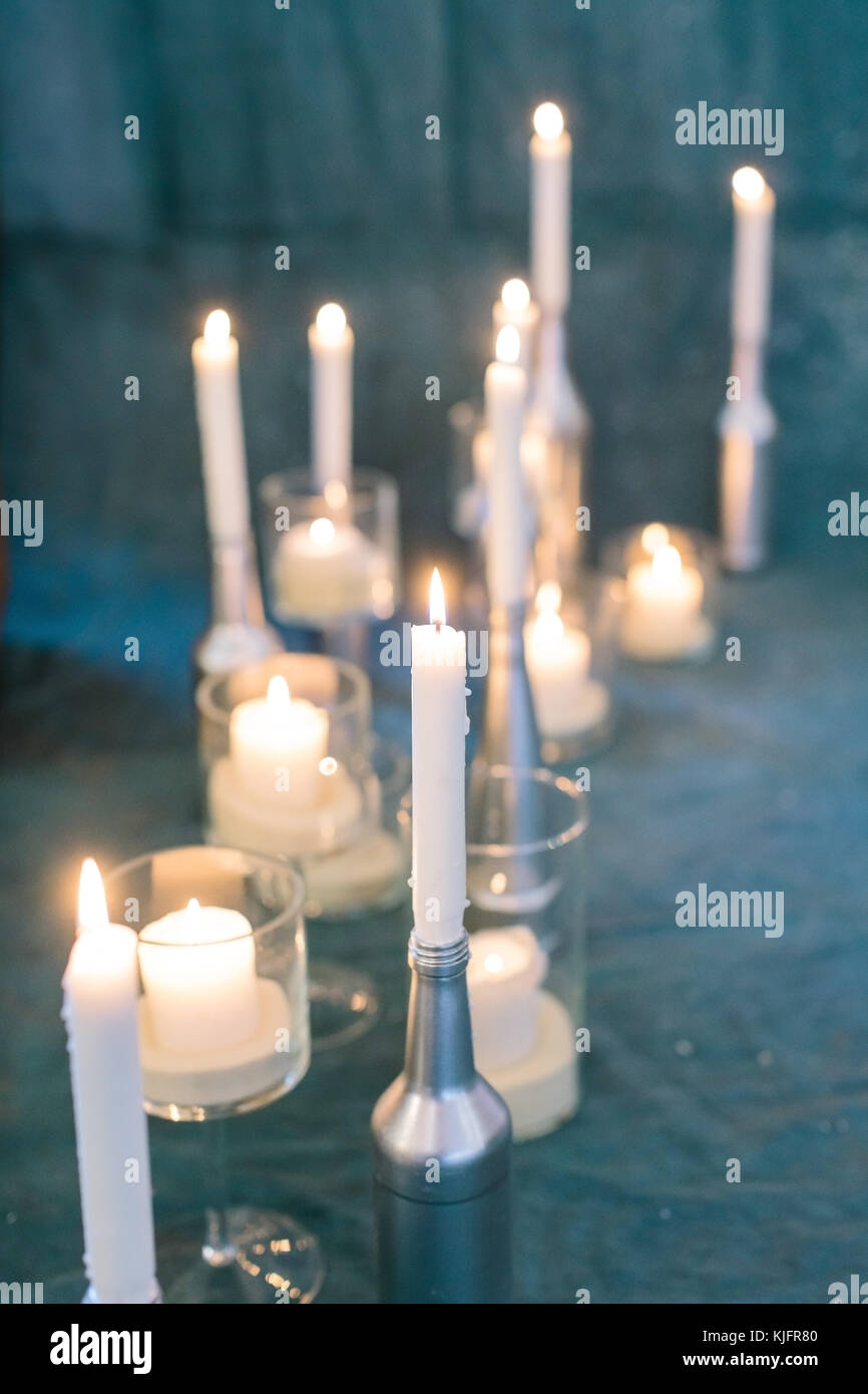 decoration, illumination, atmosphere concept. close up of burning candles of different sizes and shapes, placed on the drapping of sea blue colour Stock Photo