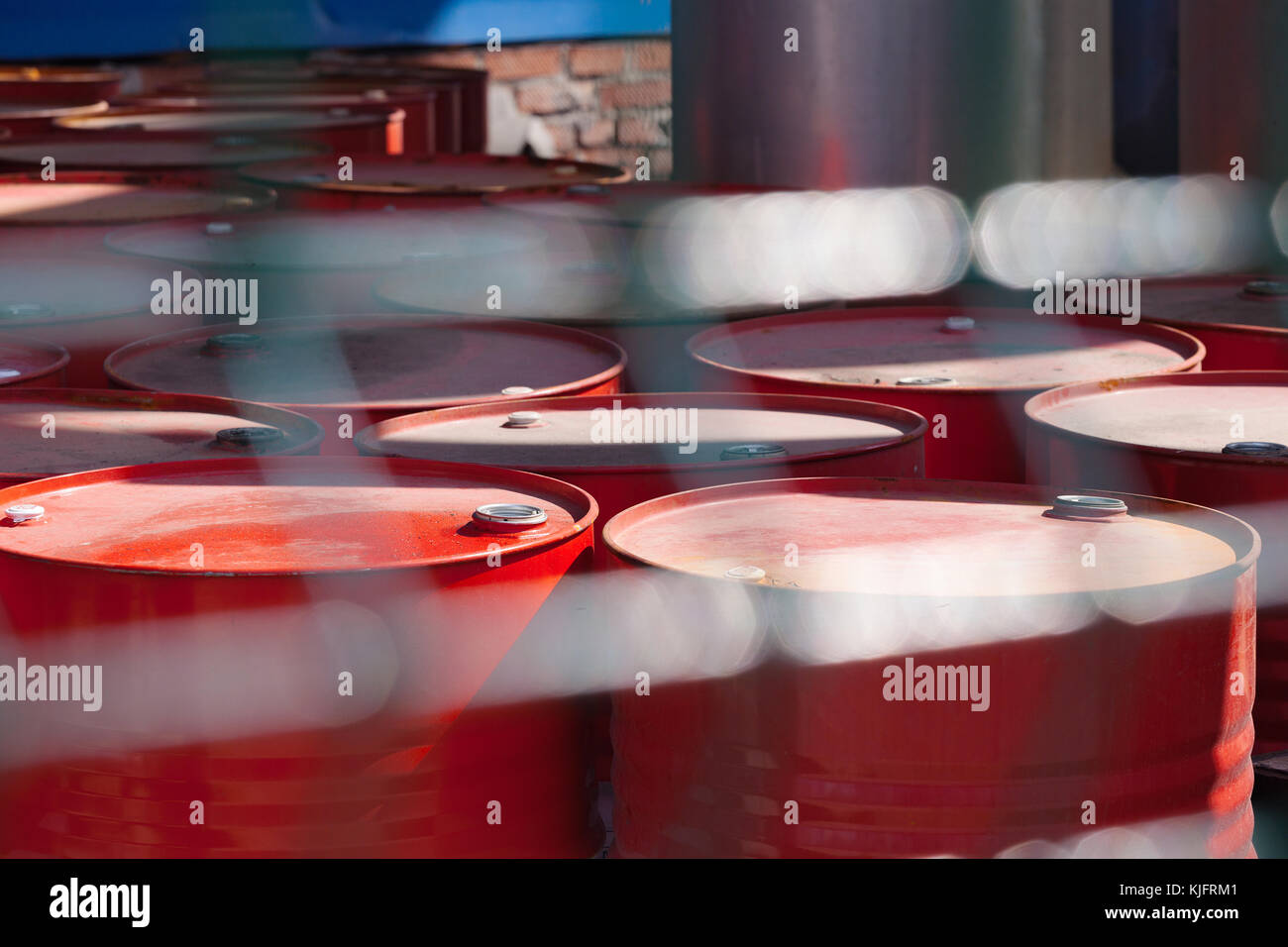 Empty red barrels in the shade of the fence. Blurred fence-grid in the foreground. Stock Photo