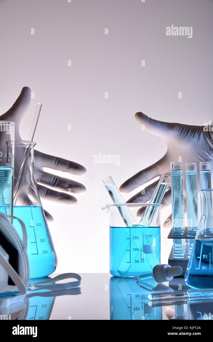 Supply of laboratory equipment with glass containers and protective elements on a table and hands with gloves in the background. Vertical composition. Stock Photo