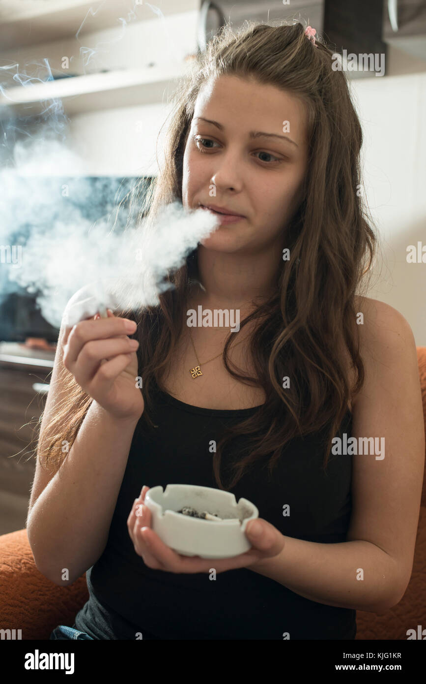 Girl smokes and holds ashtray. Smoking cigarette in the house Stock Photo