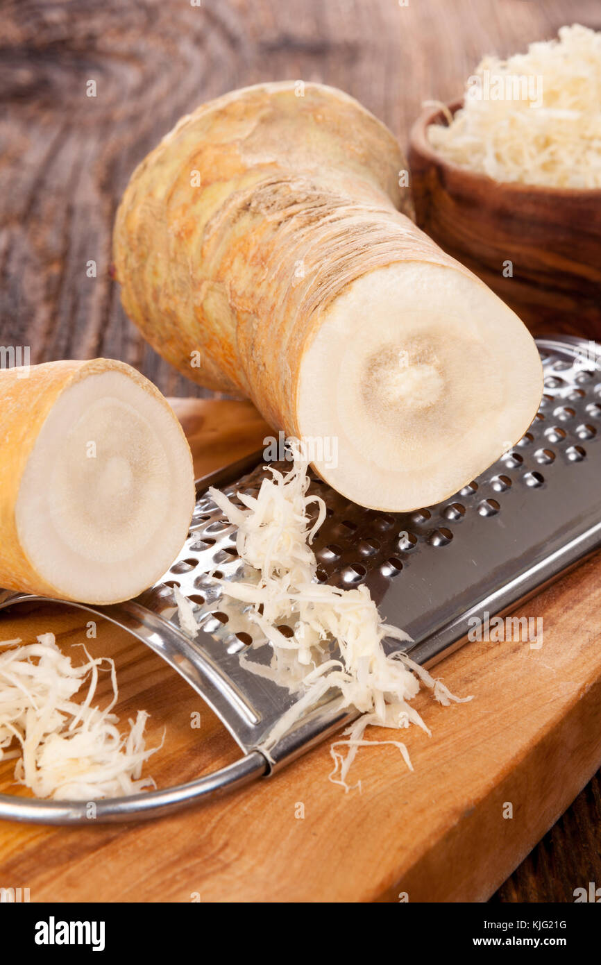 Fresh and grated horse-radish roots  in wooden bowl  on wooden background. Stock Photo