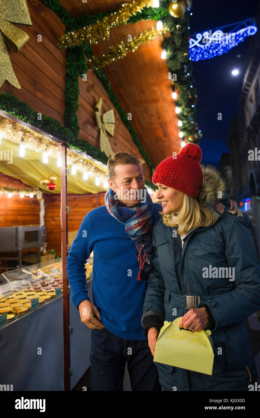 Mature couple are looking at a french pattisserie stall together in the city christmas market. Stock Photo