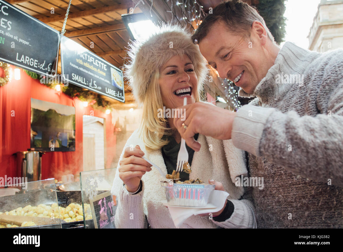 Mature couple are sharing a carton of food they have bought from a french food stall in the christmas market. Stock Photo