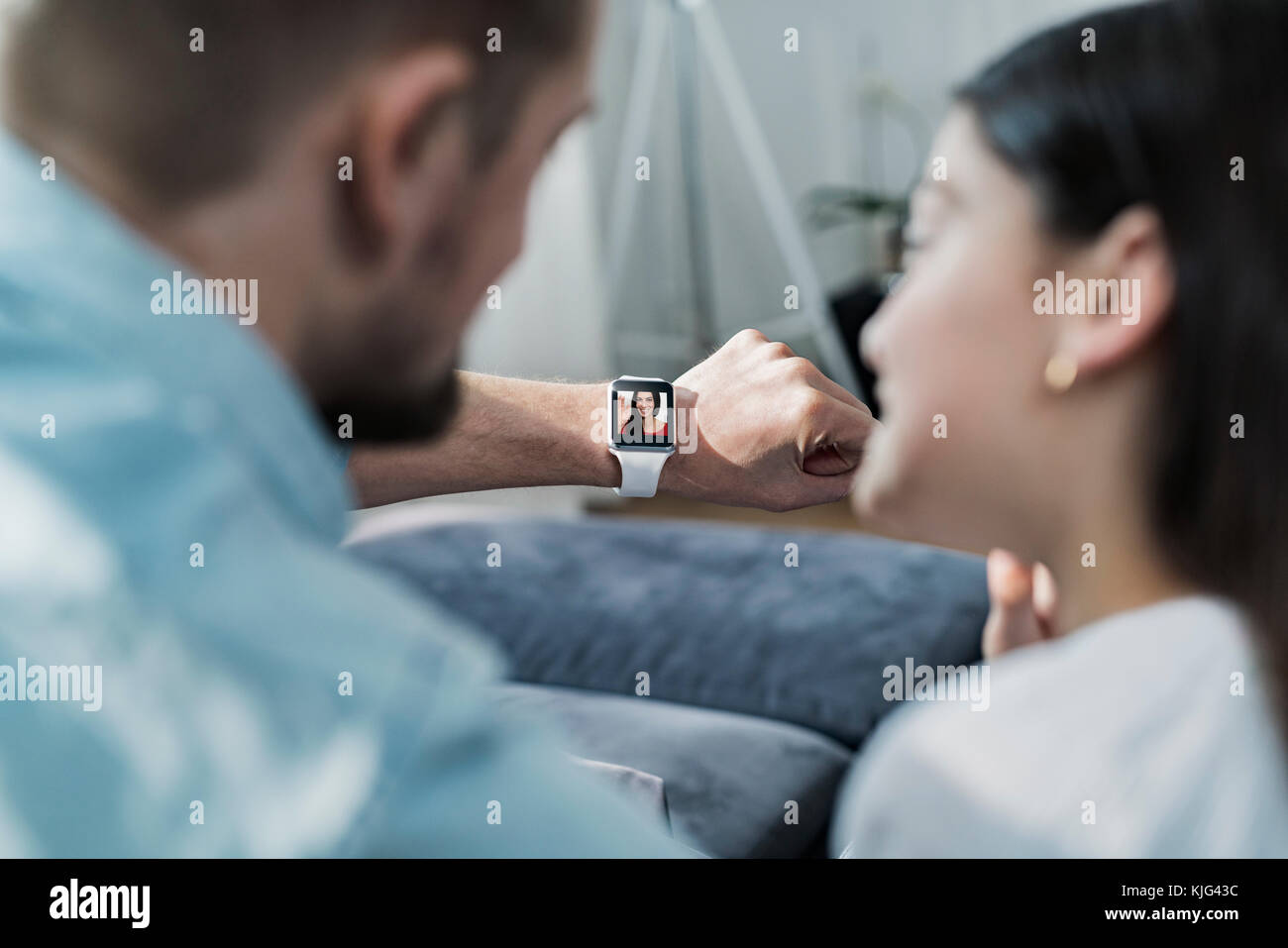 Daughter and father looking at smartwatch with mother waving at them Stock Photo