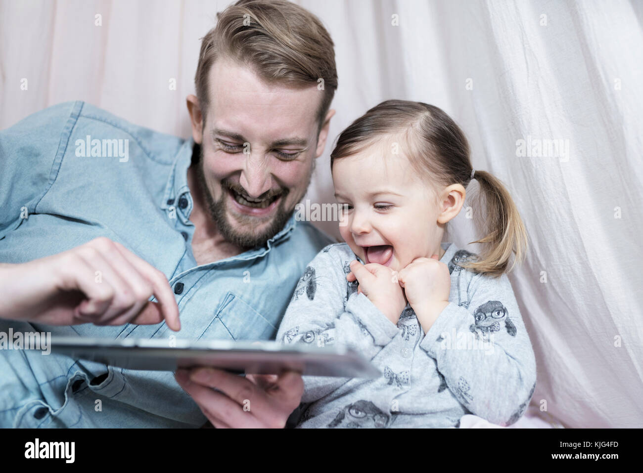 Father and his toddler daughter looking at tablet and laughing together Stock Photo