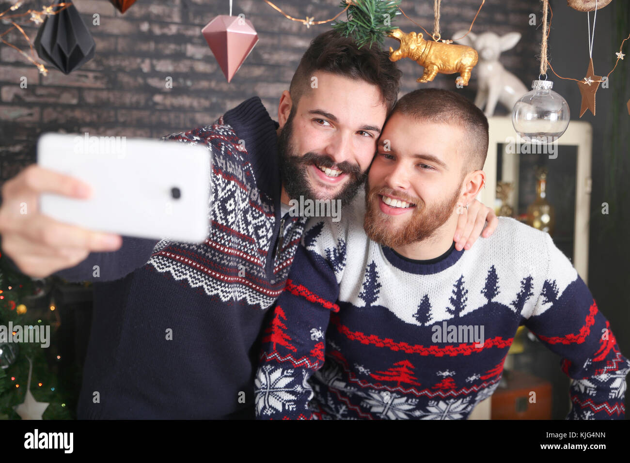 Portrait of happy gay couple taking selfie with smartphone at Christmas time at home Stock Photo